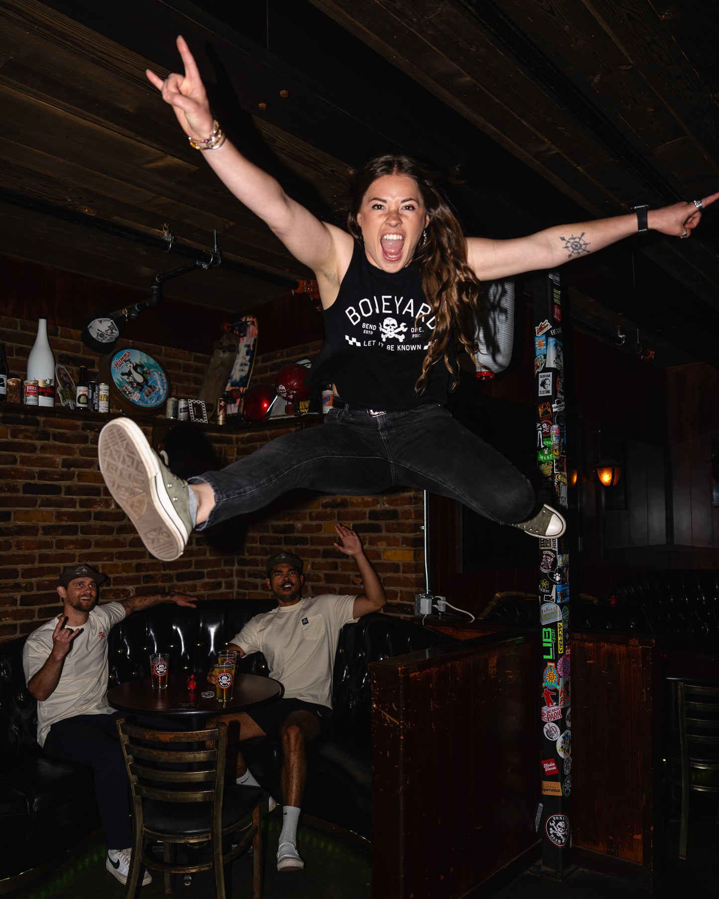 Person jumping in a bar with friends, wearing a black t-shirt with 'Boileyard' text.