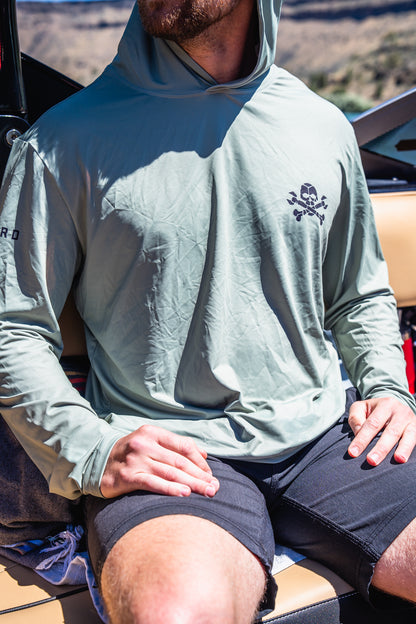 Person wearing a light gray hooded sun shirt with a logo, sitting outdoors.