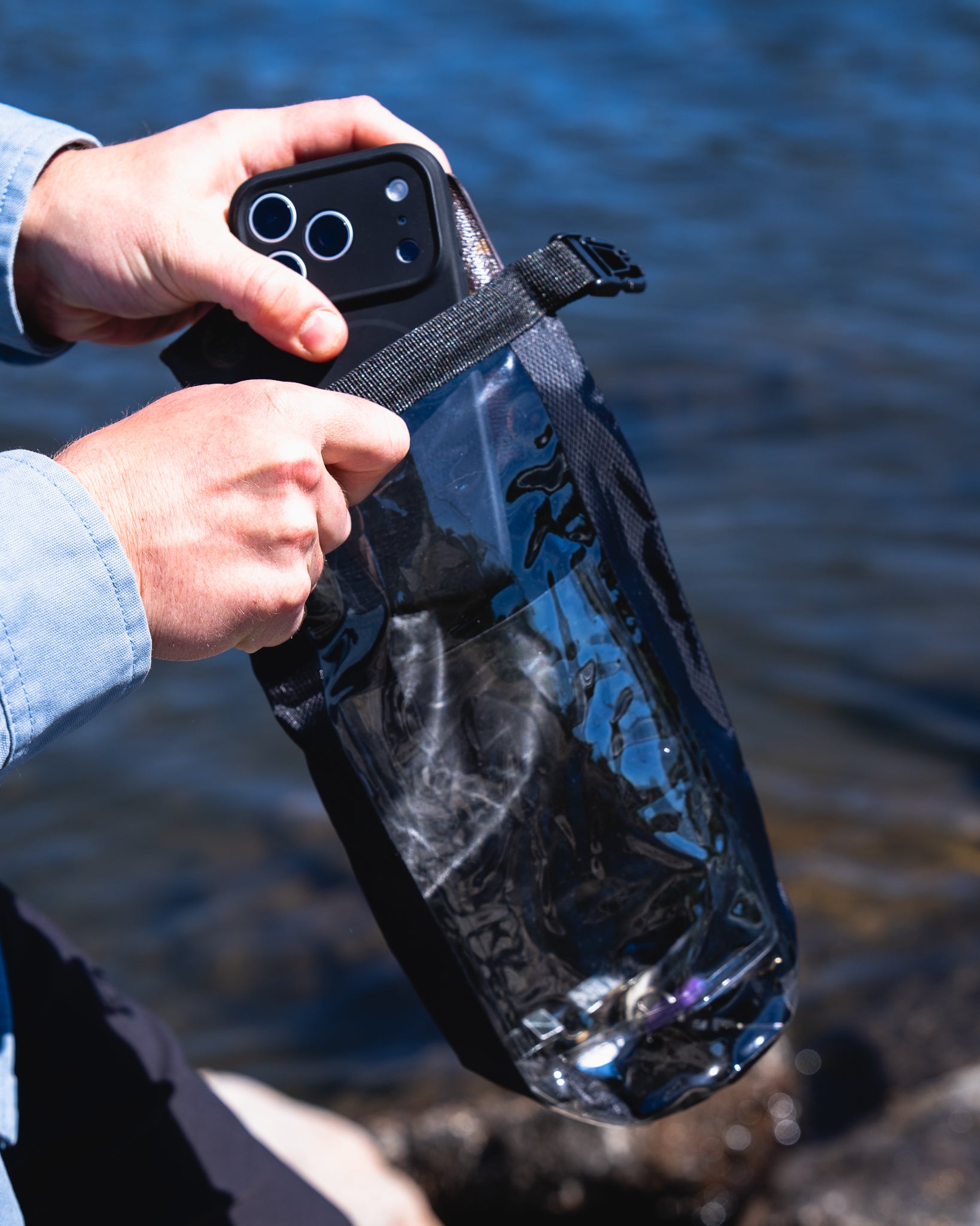 Person holding a phone in a black waterproof bag with water in the background
