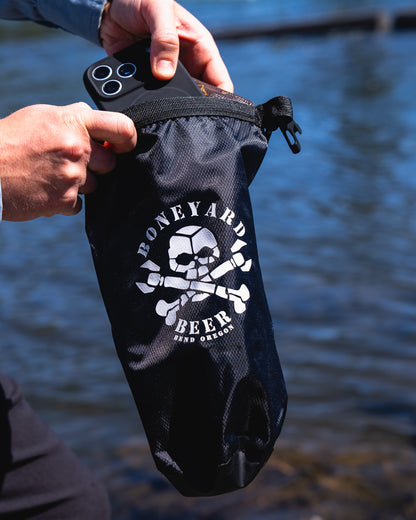 Black bag with a skull and crossbones design held by a person against a water background