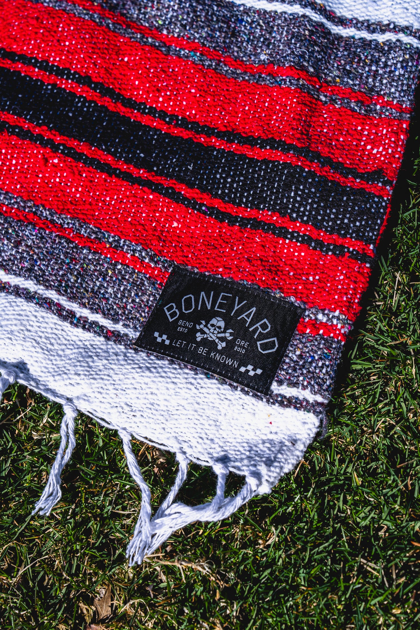 Red, black, and white striped blanket with a 'Boneyard' brand label on grass.