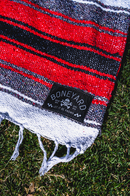 Red, black, and white striped blanket with a 'Boneyard' brand label on grass.