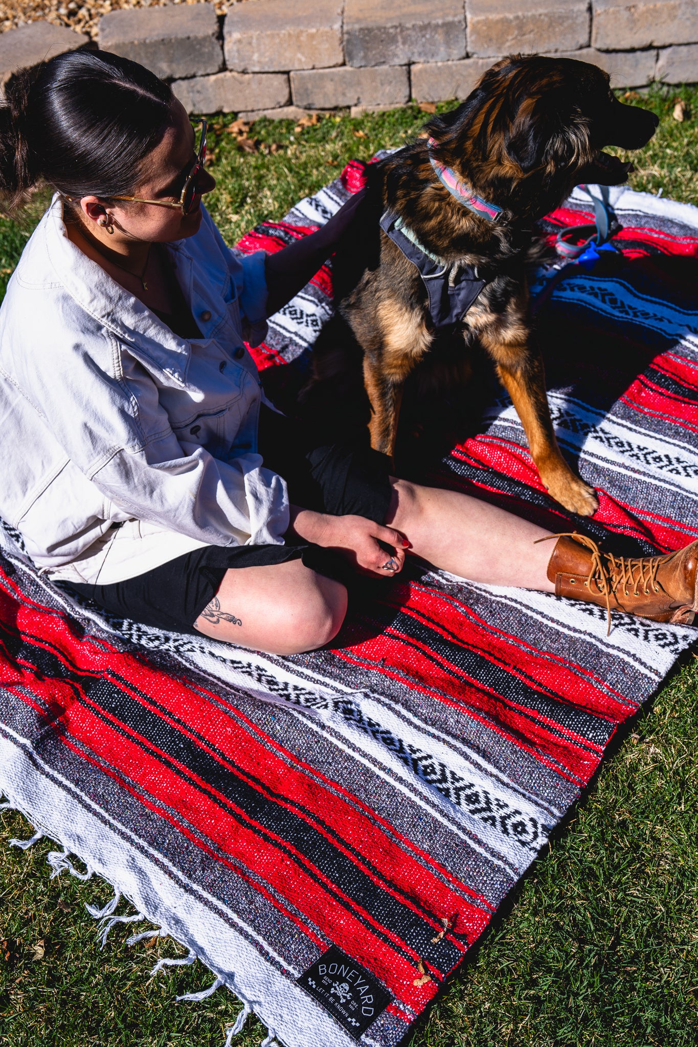 Person sitting on a colorful blanket with a dog, both on grass.