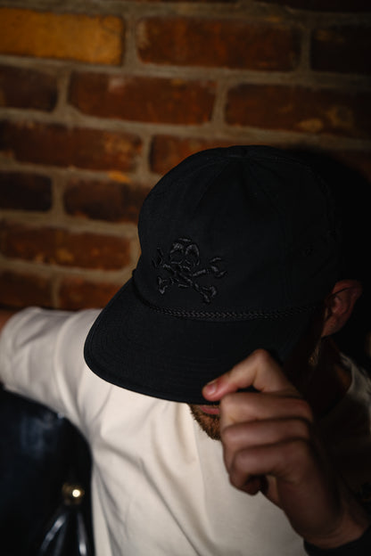 Person wearing a black cap with a logo against a brick wall.