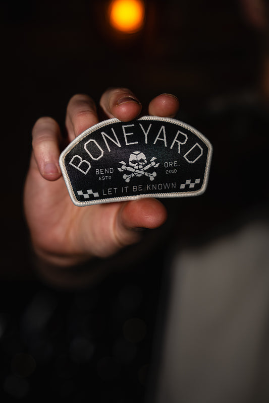 Hand holding a 'Boneyard' patch with a skull design against a dark background