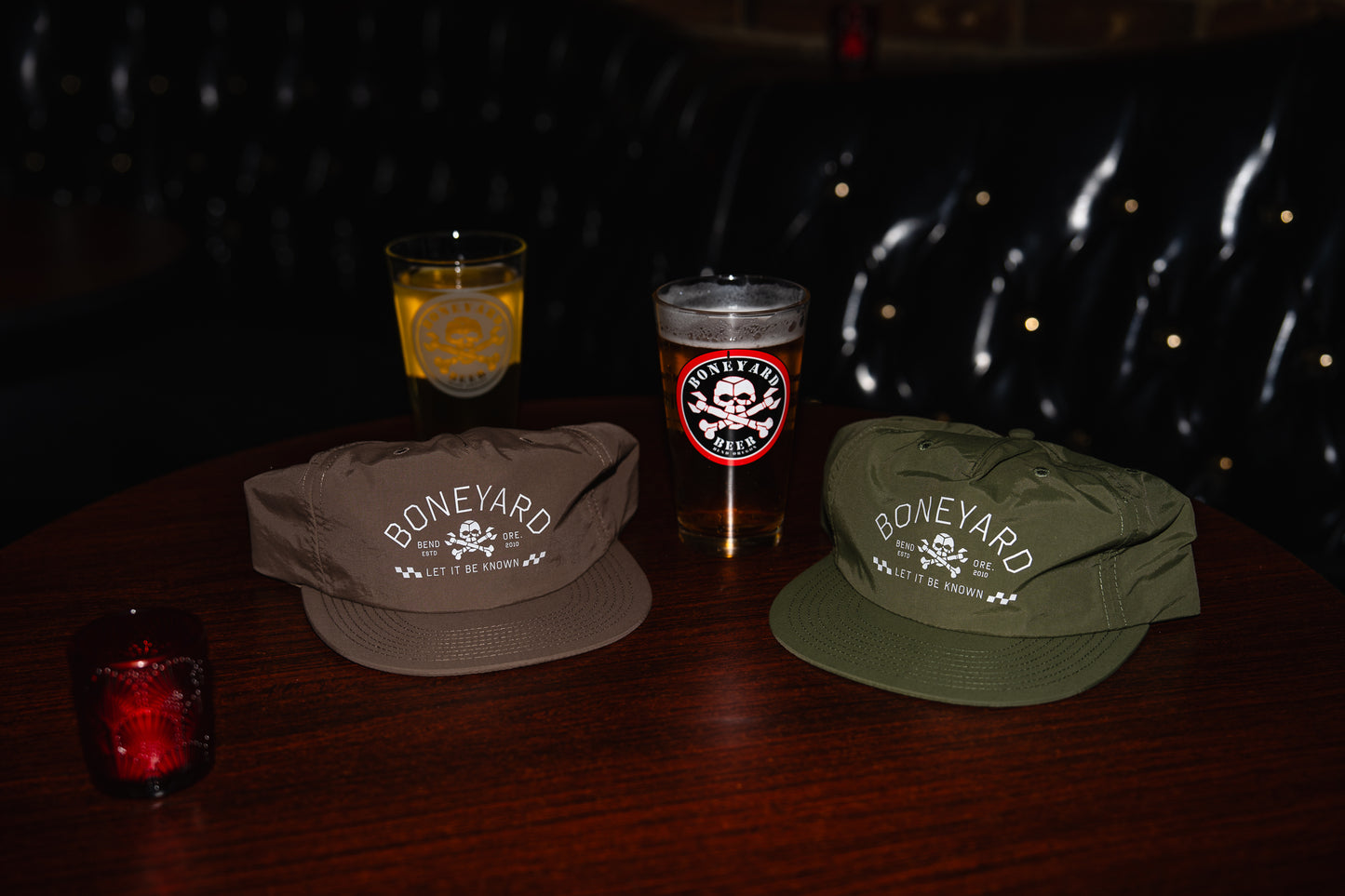 Two hats with 'Boneyard' branding on a dark surface with drinks.