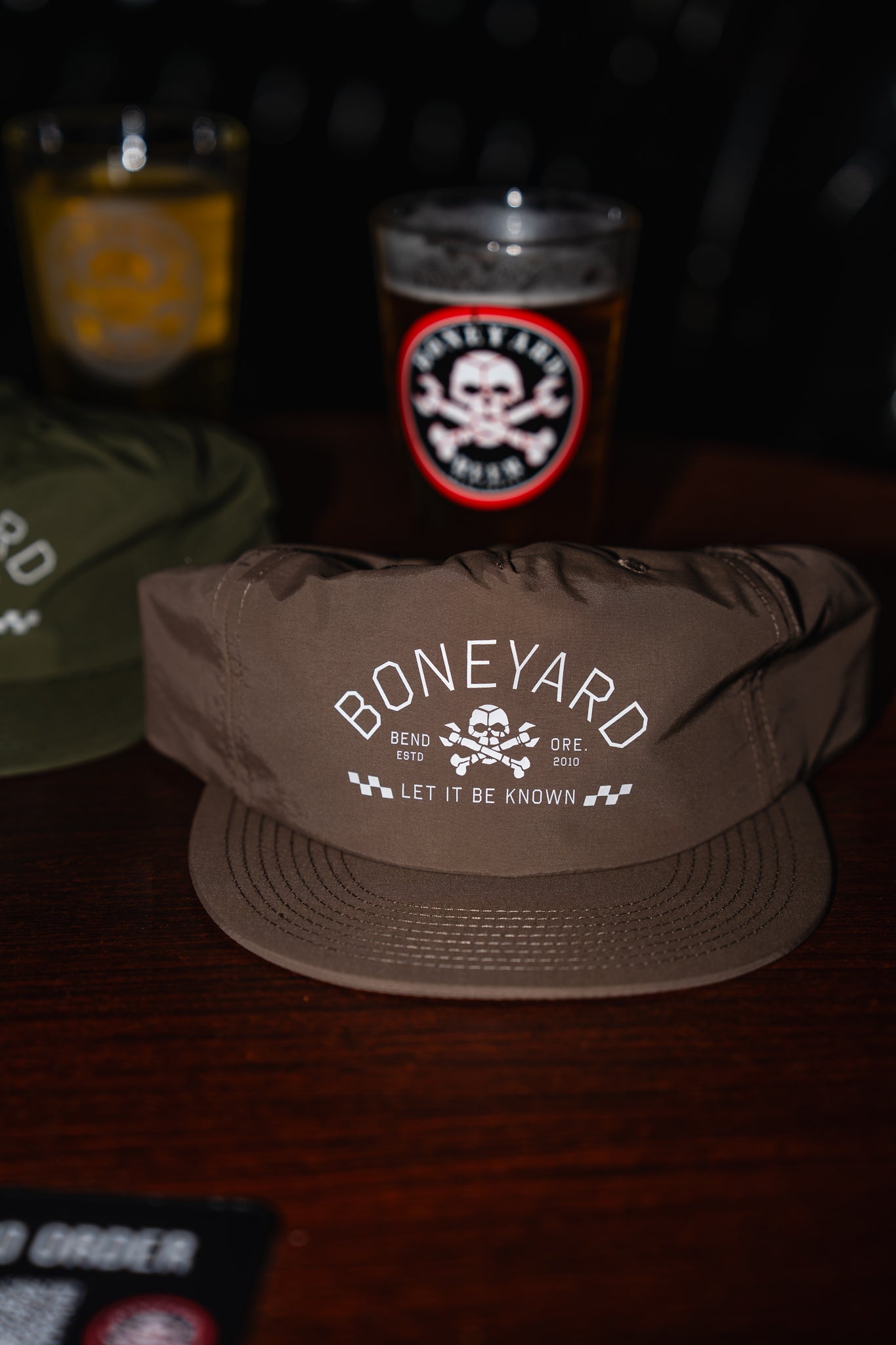 Taupe cap with 'Boneyard' logo on a dark background