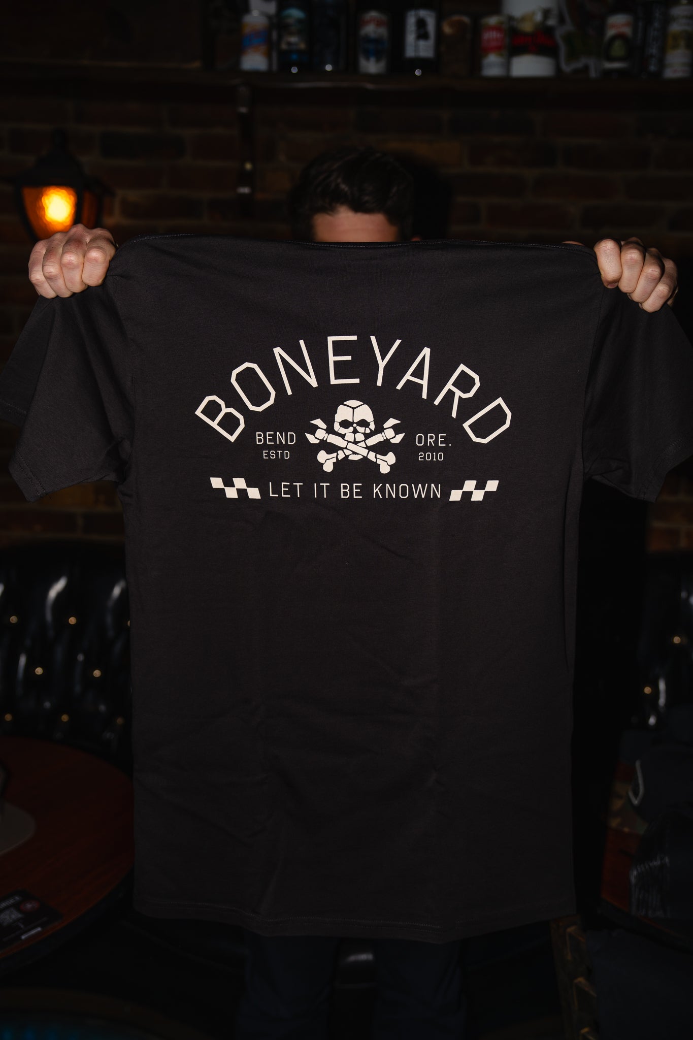 Person holding a black t-shirt with 'Boneyard' logo and text in a dimly lit room.