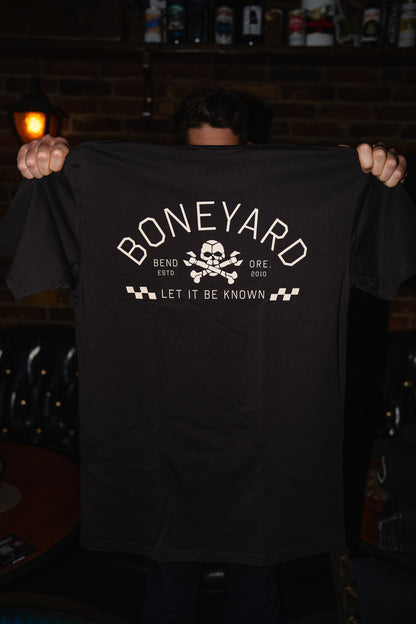 Person holding a black t-shirt with 'Boneyard' logo and text in a dimly lit room.