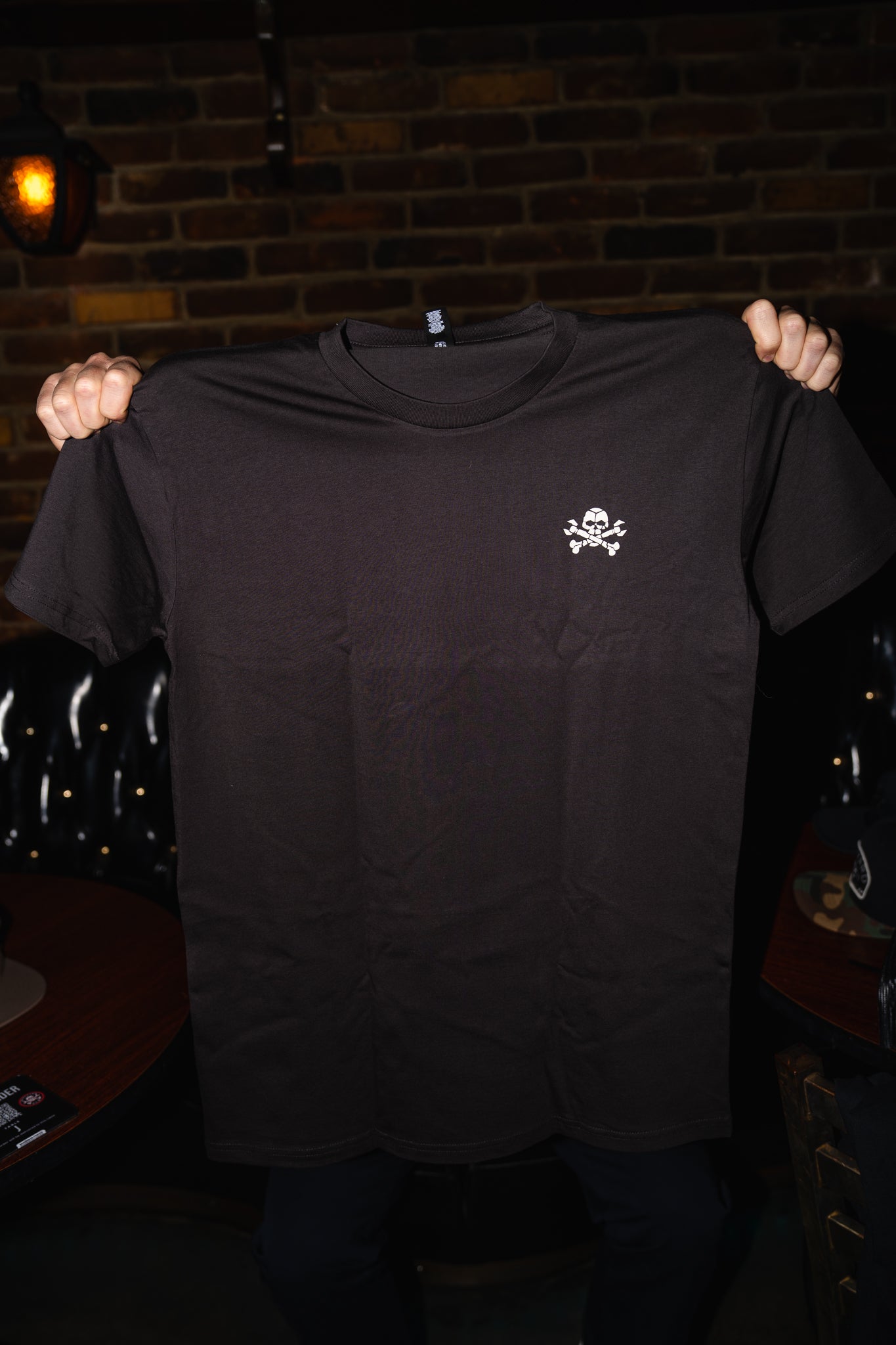 Black t-shirt with a small white logo held up against a dark background