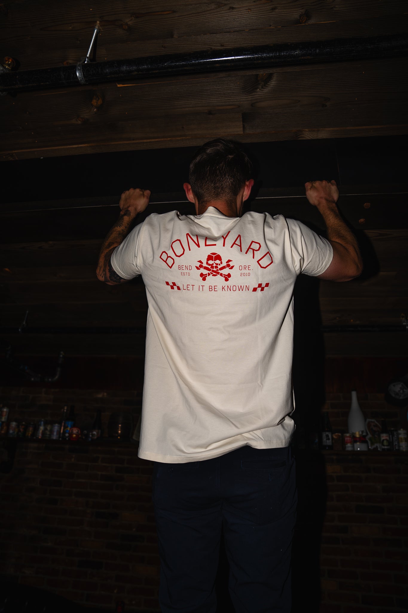 Person wearing a white t-shirt with red text and graphics, standing in a dimly lit room.