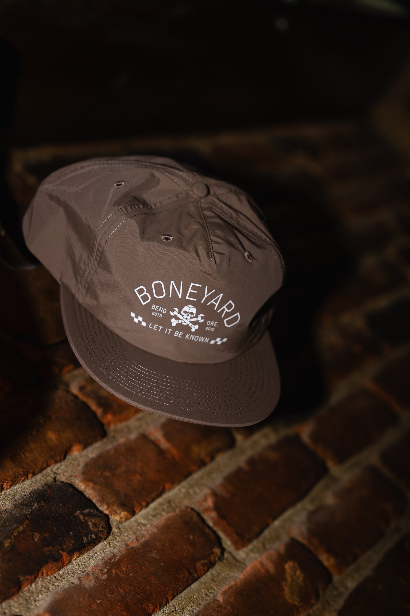 Taupe cap with 'Boneyard' logo on a brick surface