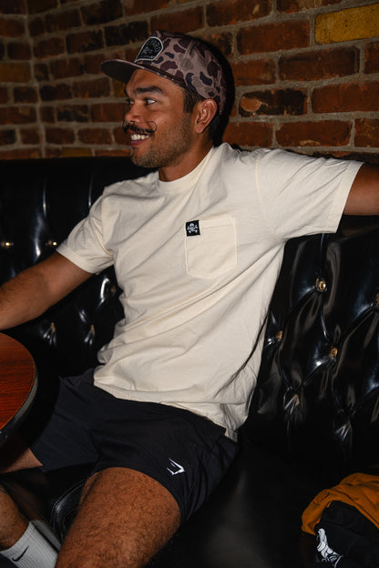 Man sitting on a black leather couch against a brick wall with a camo hat on
