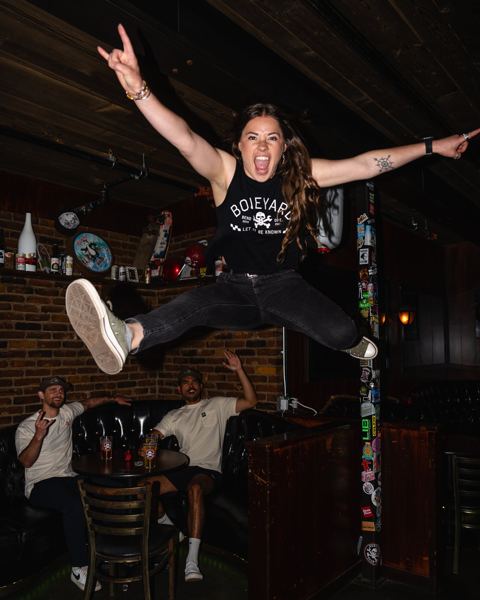 Person jumping in a bar with friends, wearing a black t-shirt with 'Boileyard' text.