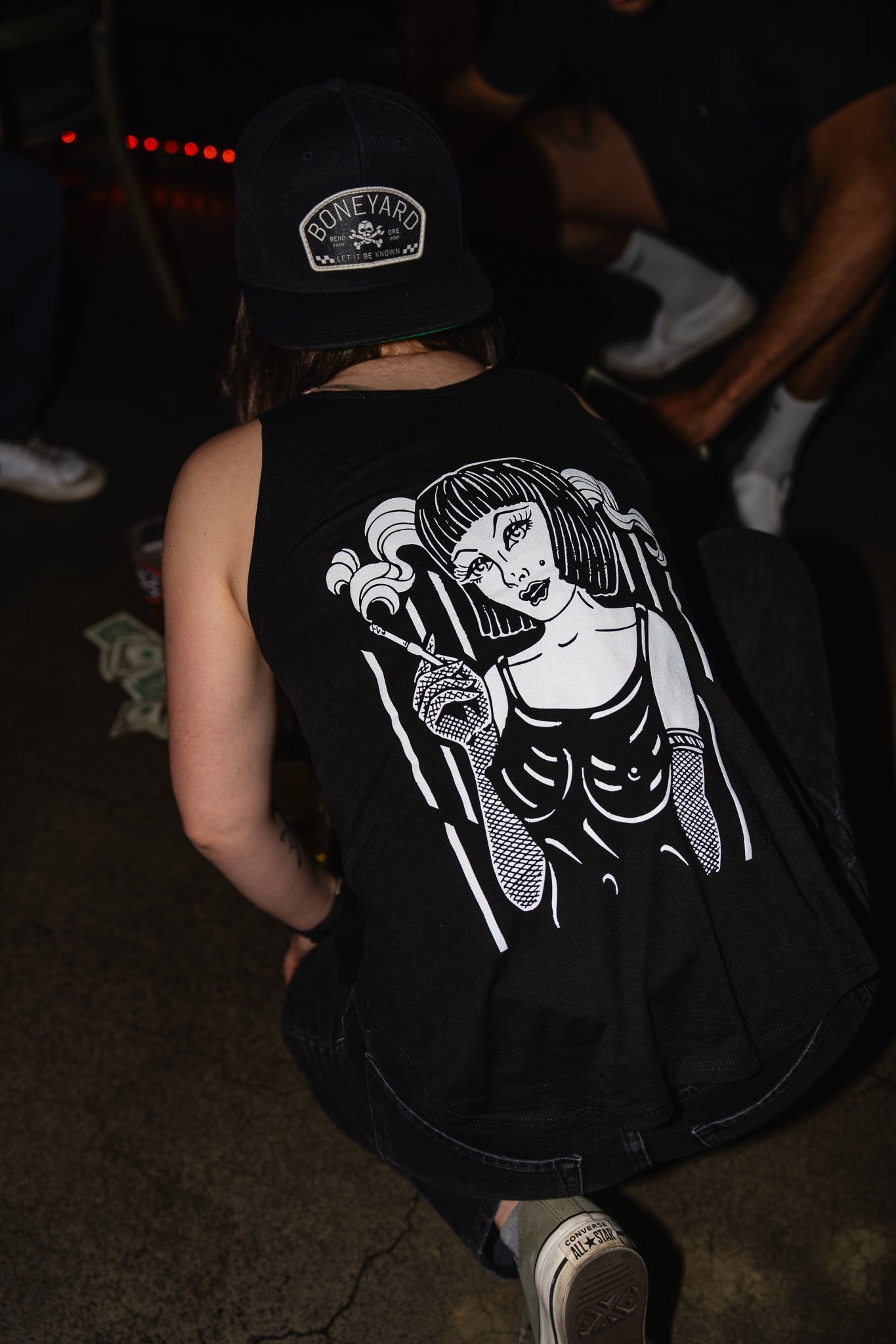 Person wearing a black sleeveless shirt with a graphic design, standing in a dark setting.