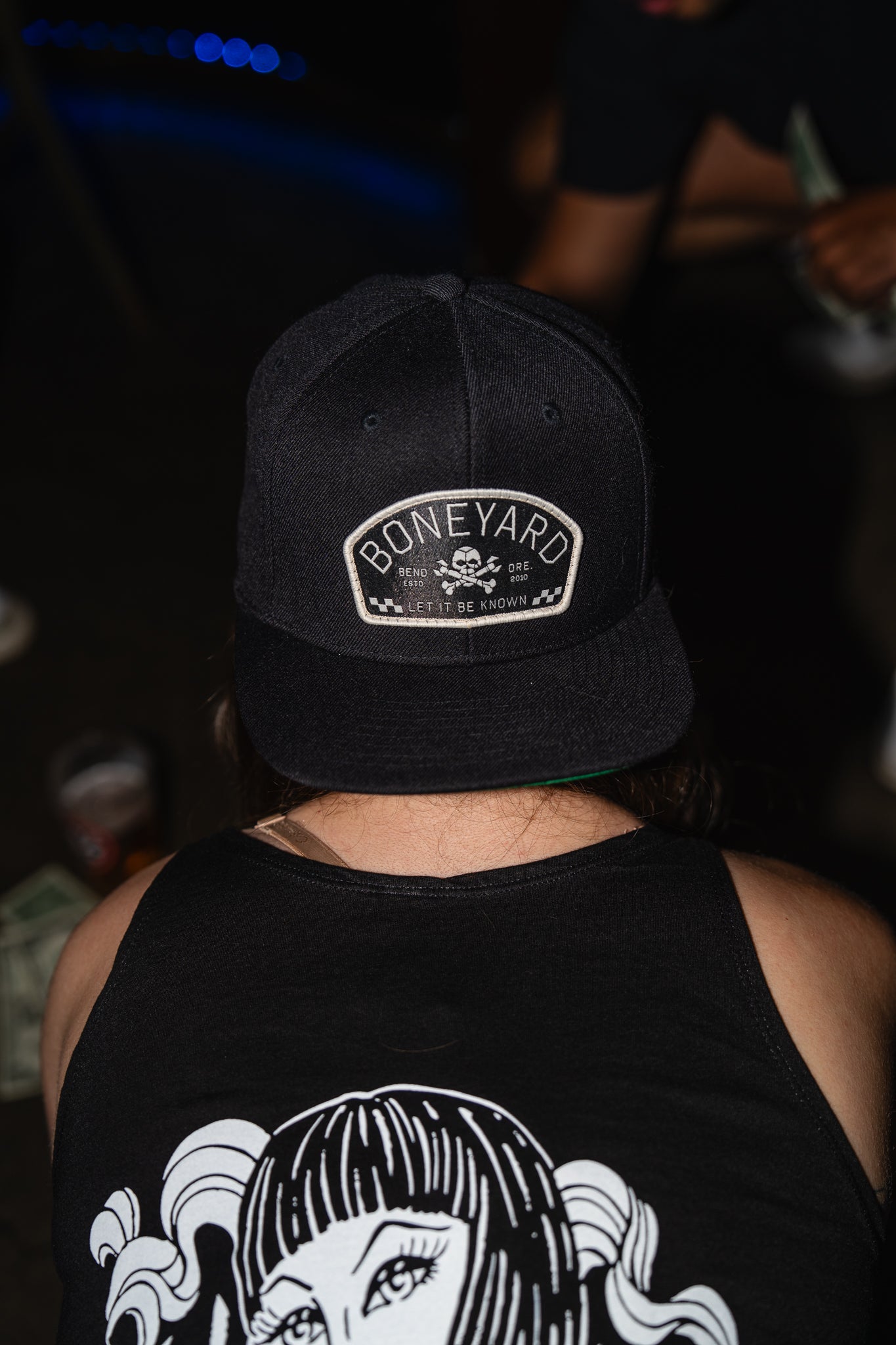 Person wearing a black cap with 'Boneyard' logo and black tank top with graphic design.