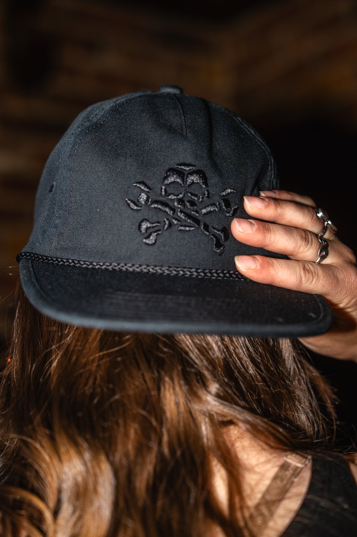 Black cap with skull and crossbones design held by a person against a dark background