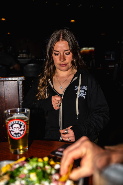 Woman sitting at a bar with a beer and food, surrounded by dim lighting