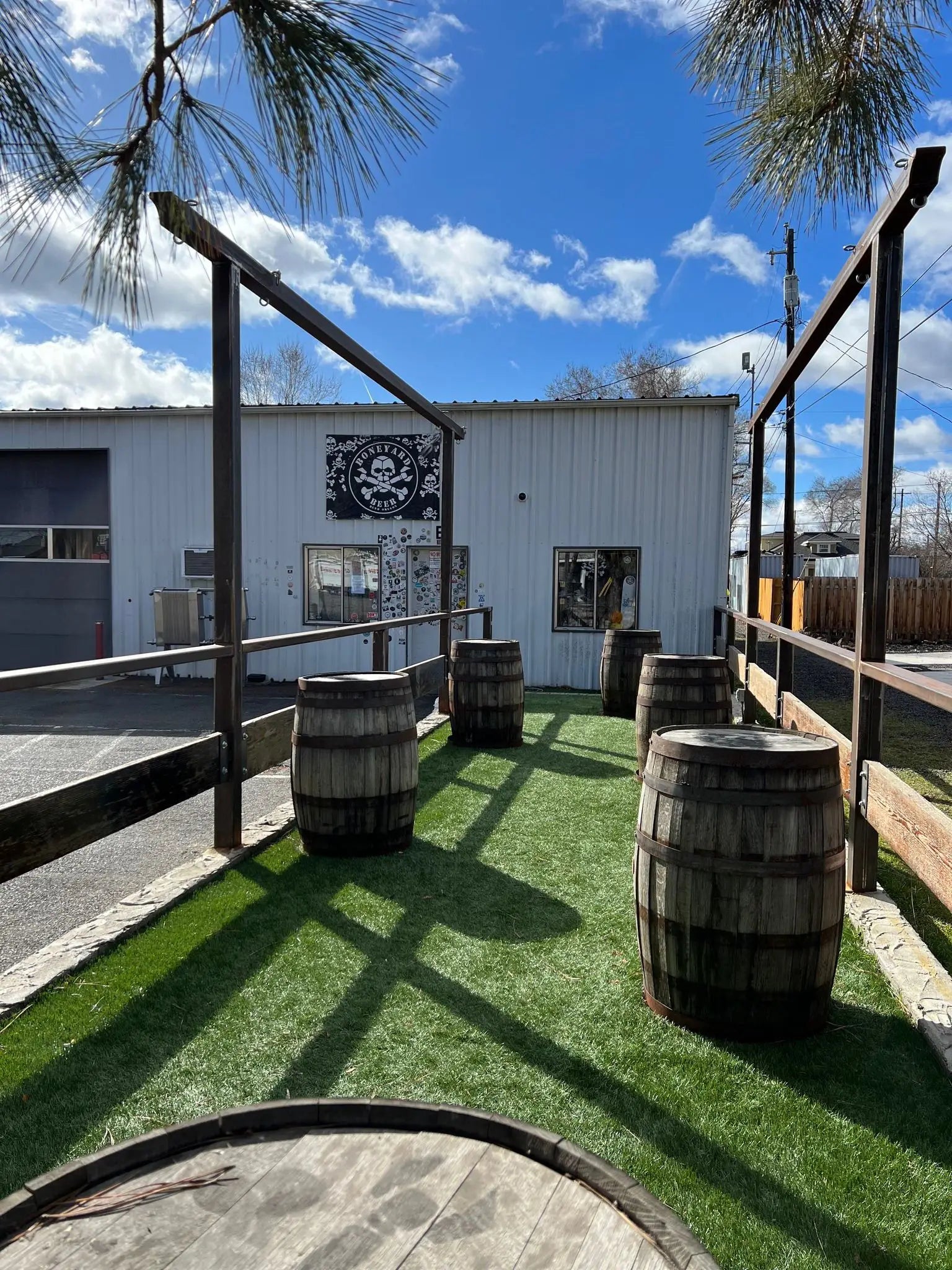 An exterior photo of the Boneyard Tasting Room showing an area where visitors can relax and enjoy beers on old barrels used as tables.